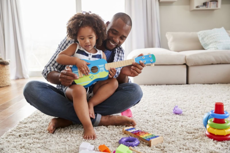 Father playing with his child with a toy guitar on the floor.