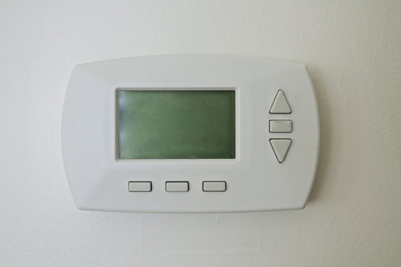 Digital thermostat mounted on a wall with a blank screen.