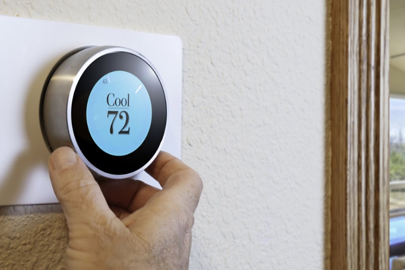 Photo of a digital thermostat mounted on a wall with a blue light.